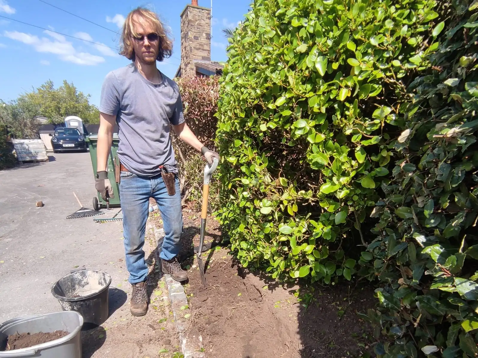 The gardener cutting a clean new edge along a hedge border beside a driveway