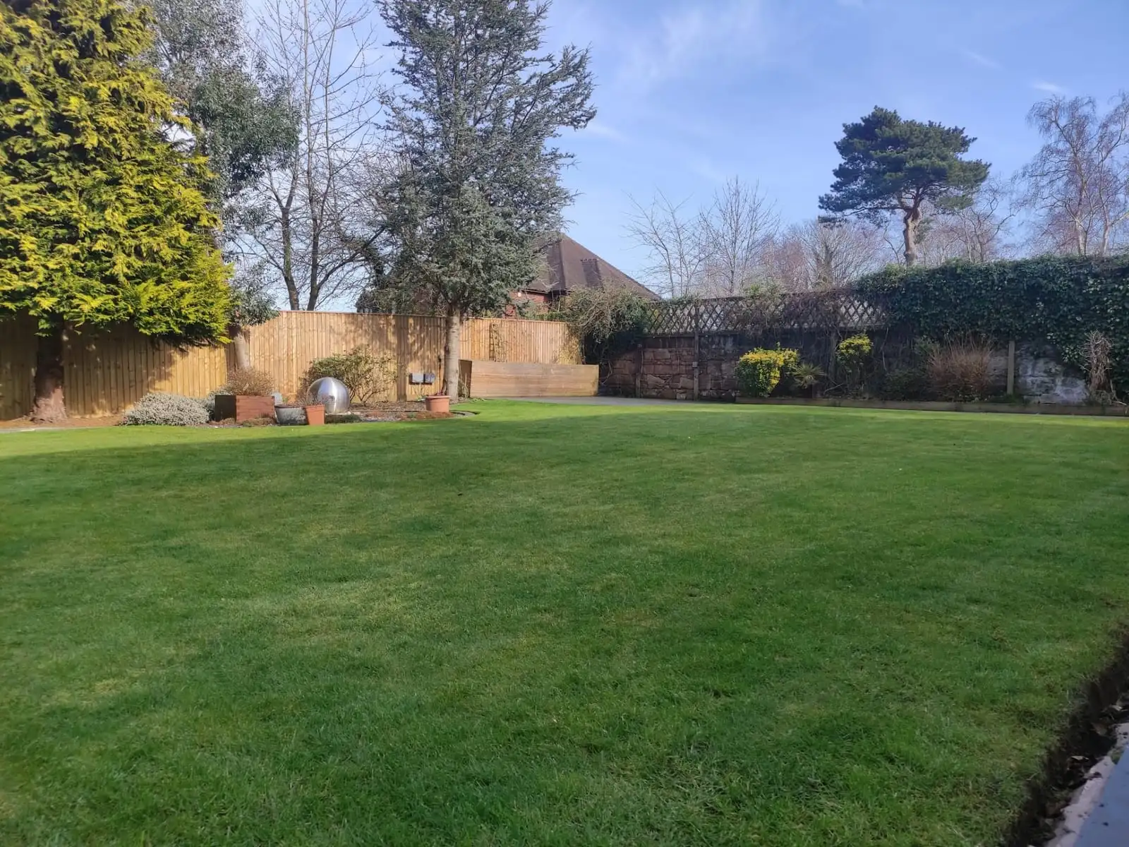 A wide, freshly mown lawn edged with shrubs, a sandstone wall and trellis