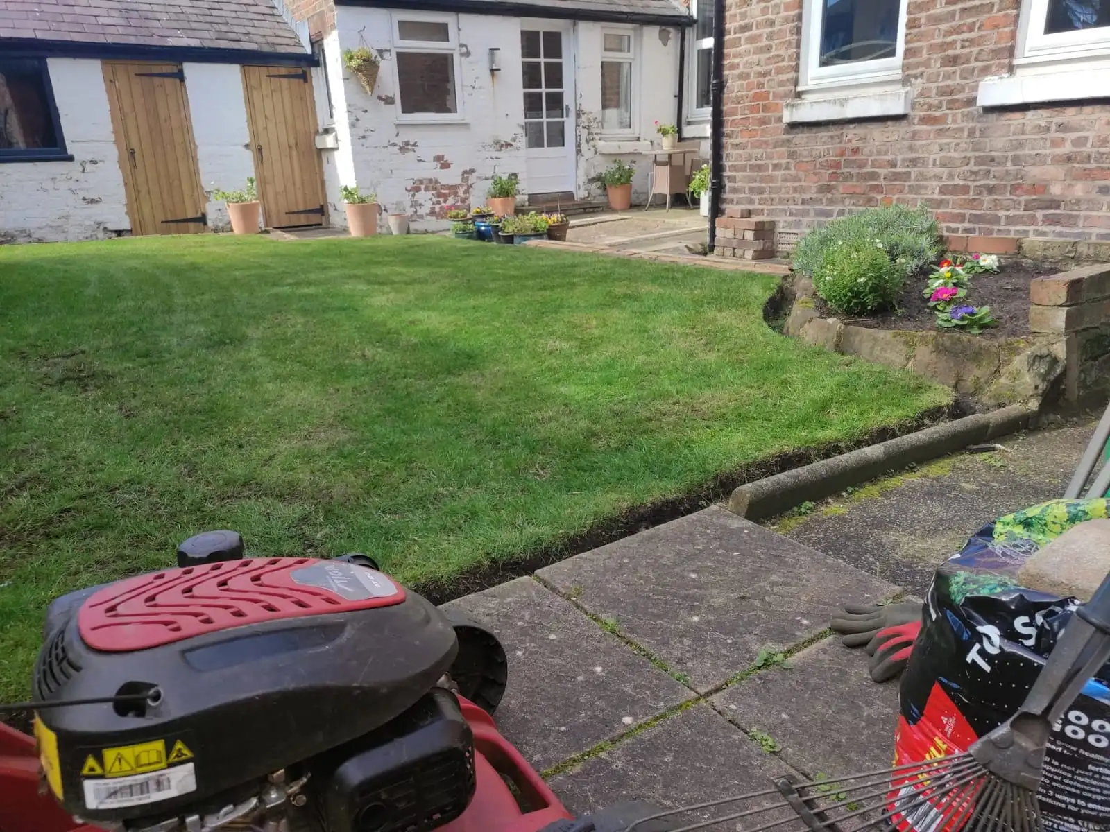 A small front lawn freshly cut and edged, with the mower and a bag of lawn feed to one side